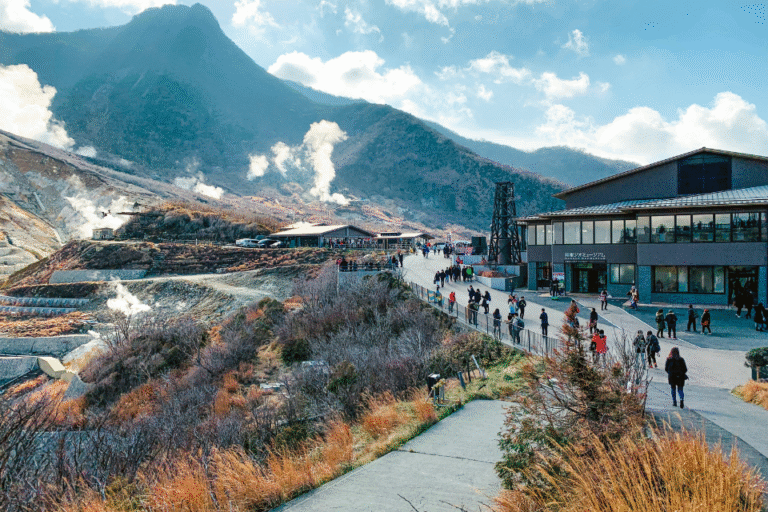 alt="Scenic view of Ōwakudani volcanic valley in Hakone, with rising steam and visitors walking along the path"