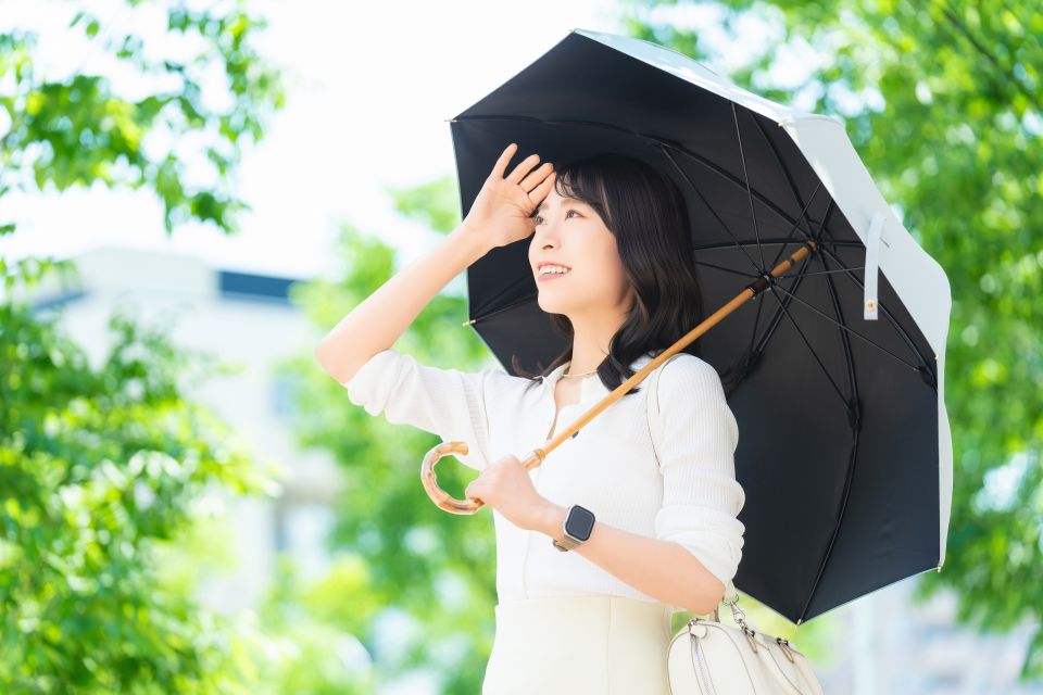 People walking with umbrellas and fans on a hot day in Tokyo